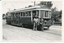 A vintage tram, numbered 22 and marked "MT. PLEASANT", stands on tracks next to a road. Two individuals, one in a khaki uniform and hat, and another, a lady conductor in a dark uniform with a cap, stand at the front of the tram. Trees and a brick fence are visible in the background.
