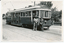 A vintage tram, numbered 22 and marked "MT. PLEASANT", stands on tracks next to a road. Two individuals, one in a khaki uniform and hat, and another, a lady conductor in a dark uniform with a cap, stand at the front of the tram. Trees and a brick fence are visible in the background.