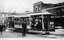 An open-air electric tram filled with passengers, with buildings lining the street and a sign on the tram reading "Gardens" and "Ballarat Tramways".