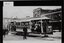 Black and white historical image of an open-air electric tram filled with passengers, with buildings lining the street and a sign on the tram reading "Gardens" and "Ballarat Tramways".