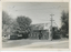 A brick building with a corrugated metal roof and the word "PRODUCE" visible on its facade, situated next to a large tree and a utility pole with overhead wires.