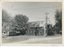 A brick building with a corrugated metal roof and the word "PRODUCE" visible on its facade, situated next to a large tree and a utility pole with overhead wires.