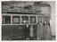 Shows a damaged section of a building wall above a vintage tram labeled with the number 24. A group of individuals stands in front of the tram, appearing to observe the damage.