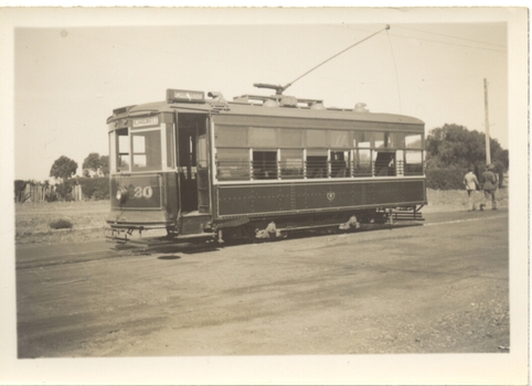 Vintage tram car numbered 30, with some open windows and a trolley on the roof, parked on tracks next to a dusty road.