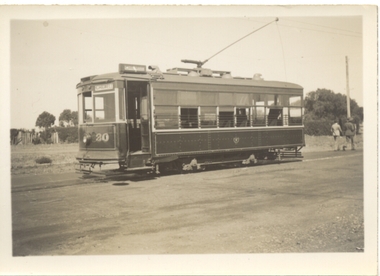 Vintage tram car numbered 30, with some open windows and a trolley on the roof, parked on tracks next to a dusty road.