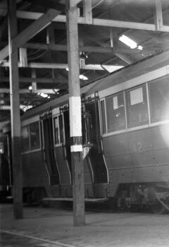 Show the side of a tramcar with multiple windows and doors, numbered 42, inside a wooden-supported structure with overhead lighting.