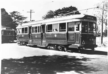 An antique tram car, labeled "SPECIAL" on its front, with multiple windows and intricate detailing, sits on a track, casting a shadow on the ground.