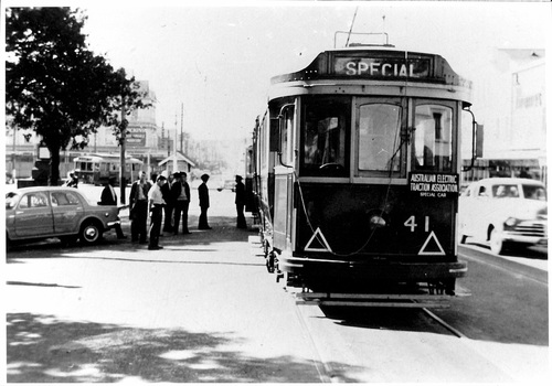 A vintage Australian electric tram numbered 41, marked "SPECIAL" on its front, stands on tracks beside a street with several parked cars and a group of people.