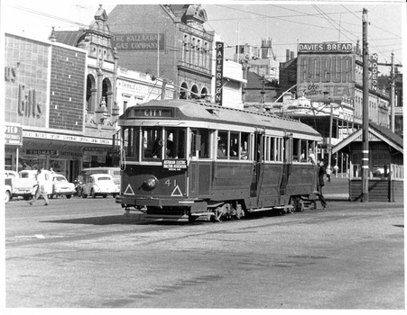 A vintage red tram numbered 41 with passengers is traveling on a city street in front of buildings with signs including "Davies Bread."