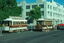 Two vintage trams, one labeled "ZOOLOGICAL GARDENS ROYAL PARK" and the other "290", and a grip cable tram are on a street in front of a light-colored building with large windows.