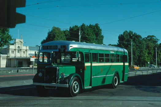 Vintage green and silver bus with "WEST MELBOURNE" displayed above the windshield, parked on a city street with a building in the background.  MMTB bus 370 in Nicholson St with part of the Exhibition buildings.