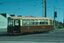 A vintage brown and tan tram numbered 676 sits on tracks with overhead power lines and poles against a bright blue sky.