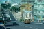 A vintage brown tram with the number 217 is traveling down a hill on a city street with multiple lanes, tram tracks, and other vehicles. Buildings line the street on both sides.