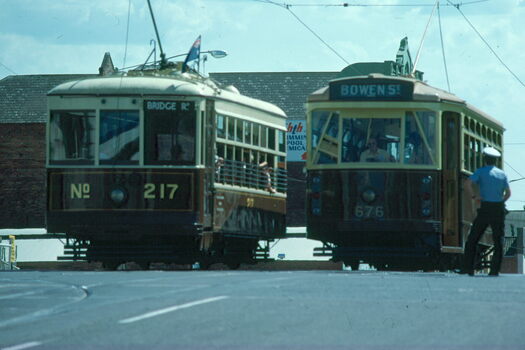 Two vintage trams, numbered 217 and 676, stand on tracks in a street scene, with one labeled "BRIDGE Rd" and the other "BOWEN ST".