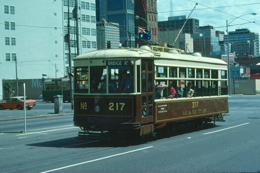 A brown and cream vintage tram with the number 217 displayed prominently, travels along a city street.