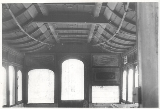 Interior view of a vintage tram car, showcasing curved wooden ceiling beams, arched windows, and decorative paneling on the walls.  