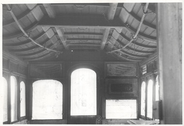Interior view of a vintage tram car, showcasing curved wooden ceiling beams, arched windows, and decorative paneling on the walls.  
