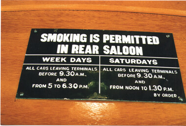 Black sign mounted on wood, stating "SMOKING IS PERMITTED IN REAR SALOON" with separate sections for "WEEK DAYS" and "SATURDAYS", detailing permitted times for tramcars leaving terminals.