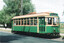 A vintage green and cream tram labeled "SPECIAL" with passengers visible through its windows, parked next to a tree-lined road.