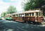 Two vintage trams, one brown with cream trim and number 661, and a green tram with cream trim, are parked on a street with trees and a banner for "Sovereign Caravans Ballarat."