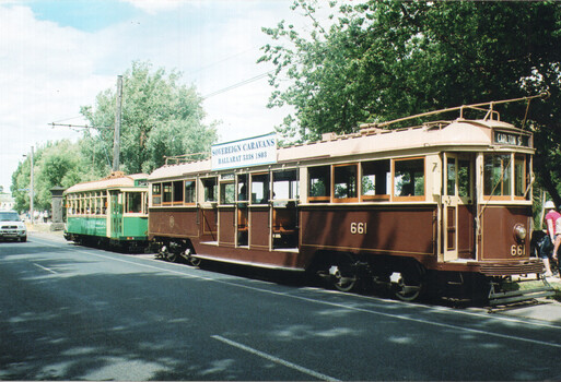 Two vintage trams, one brown with cream trim and number 661, and a green tram with cream trim, are parked on a street with trees and a banner for "Sovereign Caravans Ballarat."