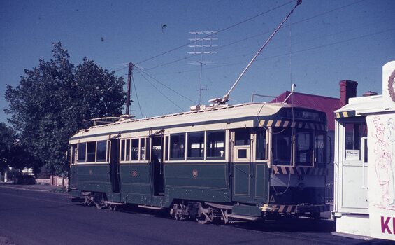 A vintage green and cream tram numbered 38 is stopped next to another tram with a cartoon drawing on the side.