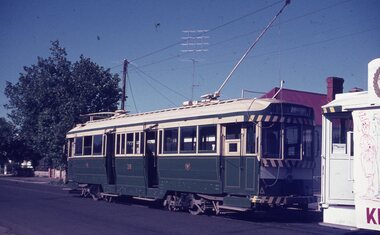 A vintage green and cream tram numbered 38 is stopped next to another tram with a cartoon drawing on the side.