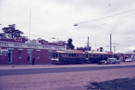 Two vintage green trams parked in front of the red brick Royal Mail Hotel, with a person standing near the entrance.