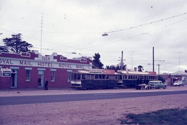 Two vintage green trams parked in front of the red brick Royal Mail Hotel, with a person standing near the entrance.