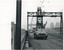 Two workers stand on a high platform attached to a lattice structure, removing overhead wires with a truck parked below on a railway track.
