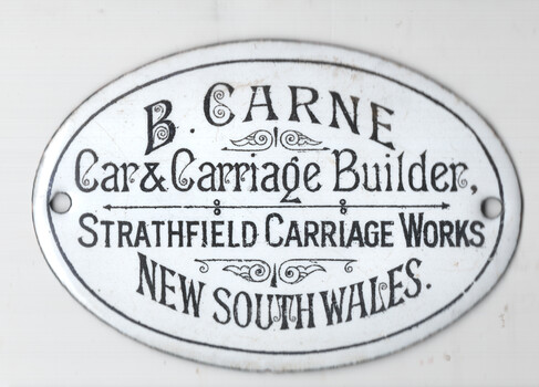 Oval enameled metal plaque with black text on a white background, reading "B. CARNE, Car & Carriage Builder, STRATHFIELD CARRIAGE WORKS, NEW SOUTH WALES."