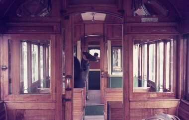 Interior of a vintage wooden tram carriage, showing seats, large windows, and arched doorways.