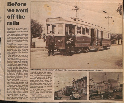 A vintage electric tram with the number 36 on its front, stopped on a track near a city center, with two uniformed staff members standing beside it.