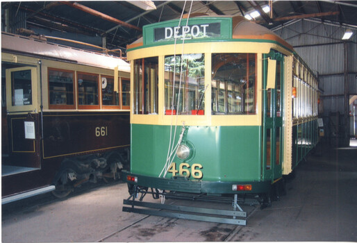 Two vintage trams, one green with destination sign "DEPOT" and number 466, parked inside a depot building.