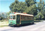 A vintage green and cream tram with "SPECIAL" signage on the front sits on tracks beside a road, with lush green trees in the background under a clear sky.