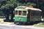 A green and yellow vintage tram labeled "ST. AIDANS DRIVE" and "466" on tracks in a park-like setting with trees and a directional sign.