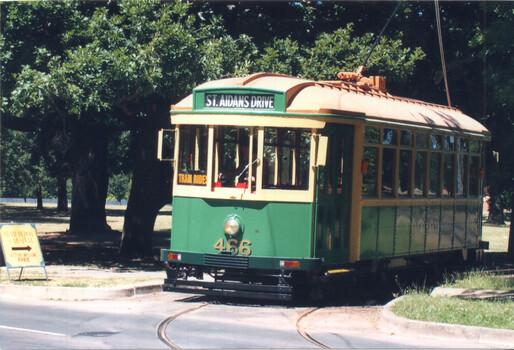A green and yellow vintage tram labeled "ST. AIDANS DRIVE" and "466" on tracks in a park-like setting with trees and a directional sign.