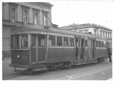 A vintage tramcar numbered 22 with open doors sits on a street in front of ornate, historic buildings.
