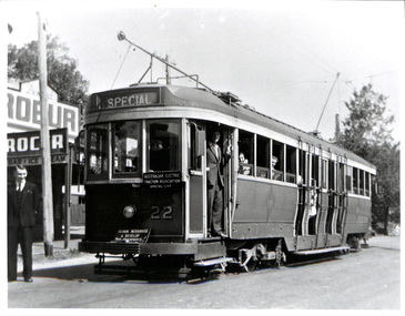 A vintage electric tram, numbered 22 and labeled "SPECIAL," stands at a stop with passengers visible through its windows.
