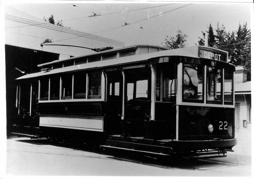 Vintage dark-colored tramcar with white trim, number 22 on the front, and "DEPOT" sign on the roof, parked indoors with overhead wires visible.
