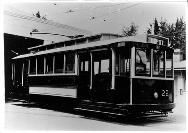 Vintage dark-colored tramcar with white trim, number 22 on the front, and "DEPOT" sign on the roof, parked indoors with overhead wires visible.