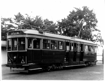 Vintage dark-colored tramcar labeled "SPECIAL" with the number 43 visible on its front, parked on a paved surface with trees in the background.