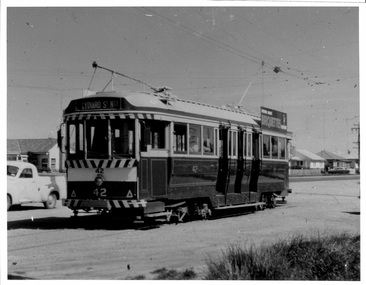 A vintage tram, numbered 42, on a street, with "LYDIARD ST Nth" displayed on its front. The tram has multiple windows and appears to be in operational condition. In the background, there are low-rise buildings and a light-colored vehicle.