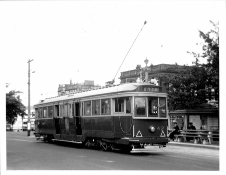 A vintage electric tram numbered 42, with "MT. PLEASANT" displayed on its front, travels on a city street next to a covered waiting shelter with benches.