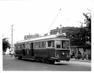 A vintage electric tram numbered 42, with "MT. PLEASANT" displayed on its front, travels on a city street next to a covered waiting shelter with benches.