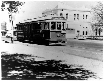 A vintage electric tram with the number 43 prominently displayed, travels along a city street past a white building and a tree casting shadows.