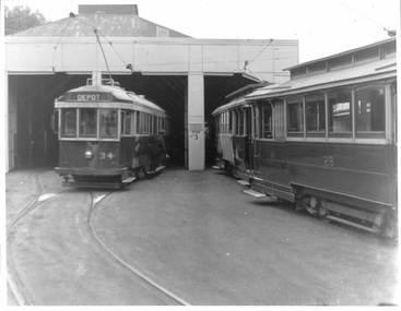 Two vintage tramcars parked in a depot with one car numbered 34 and the other numbered 28.