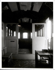 Interior view of an old-fashioned tram car, showing rows of windows and doors leading to other compartments.