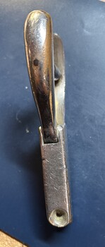 A chrome-plated metal object, with a curved handle and a rectangular base showing wear.