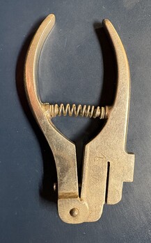 A metal ticket punch tool with a coiled spring mechanism and two curved jaws.